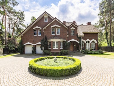 Front view of a driveway with a round garden and big, english style house in the background. Real photo
